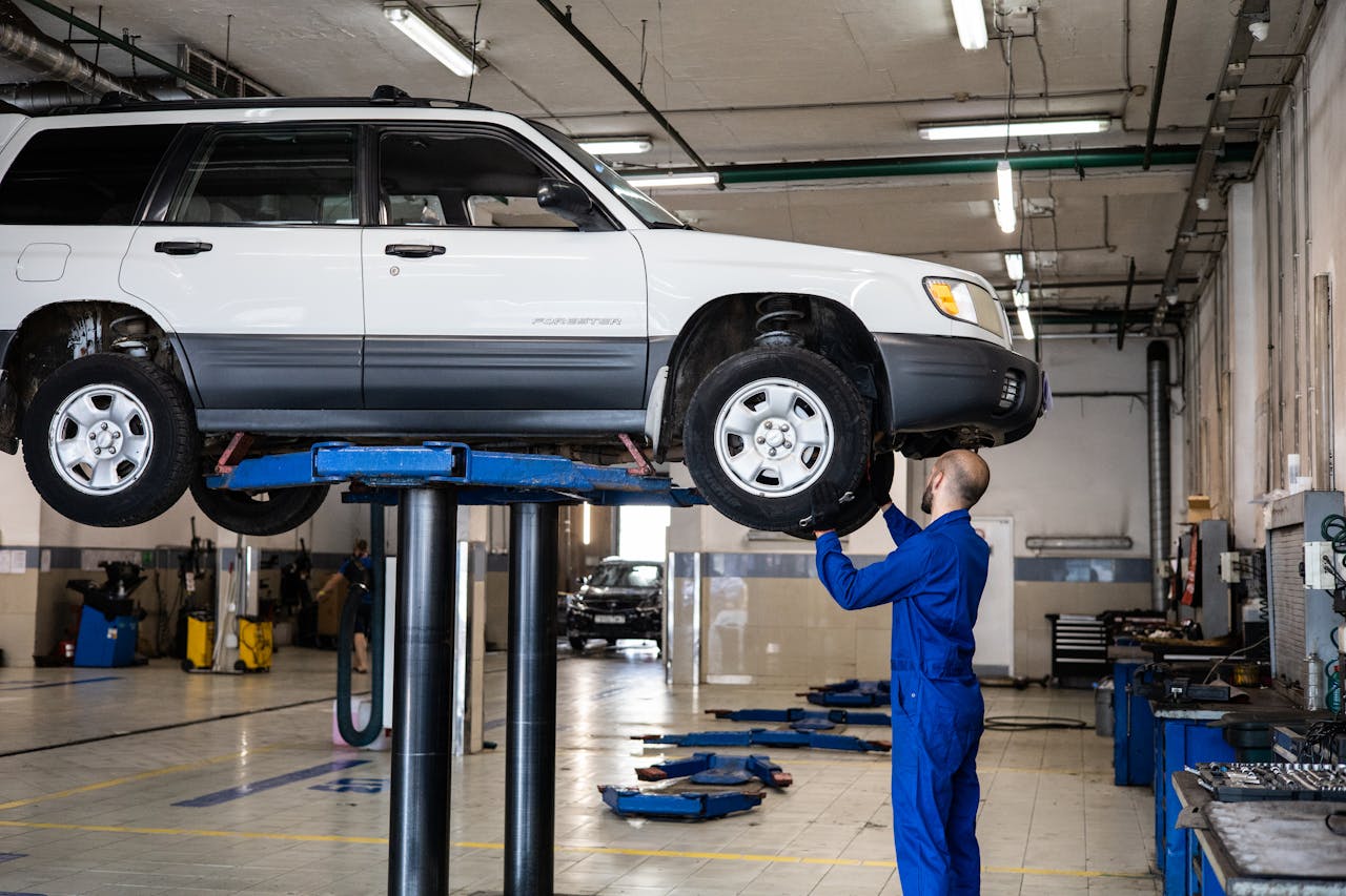services-img-04 A mechanic inspecting a white SUV lifted in a well-lit auto repair shop.